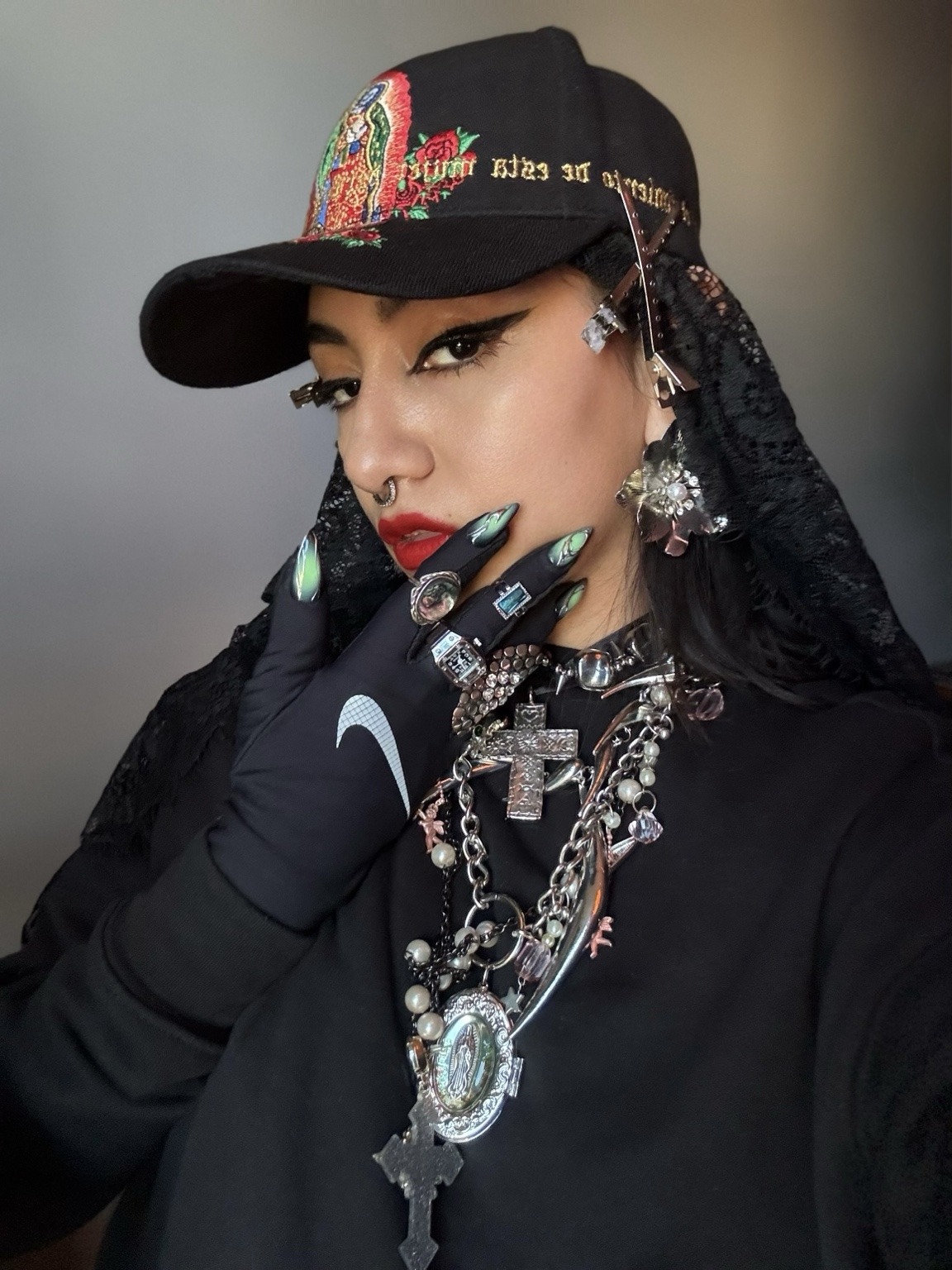 Retrato de Dixy Rodríguez con gorra bordada, encaje negro y collares, cruces y anillos plateados.