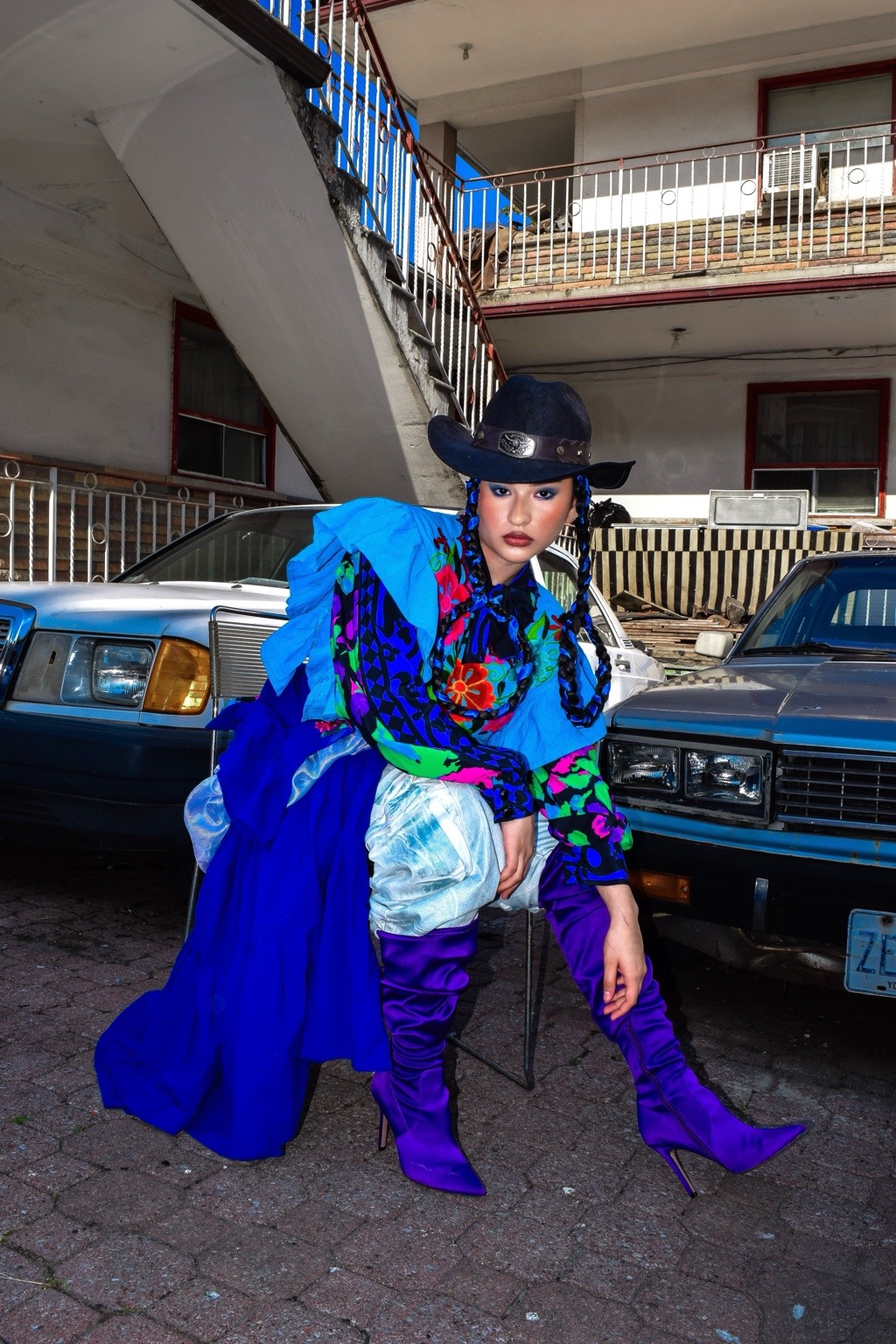 Modelo con un look azul y botas moradas frente a dos automóviles.