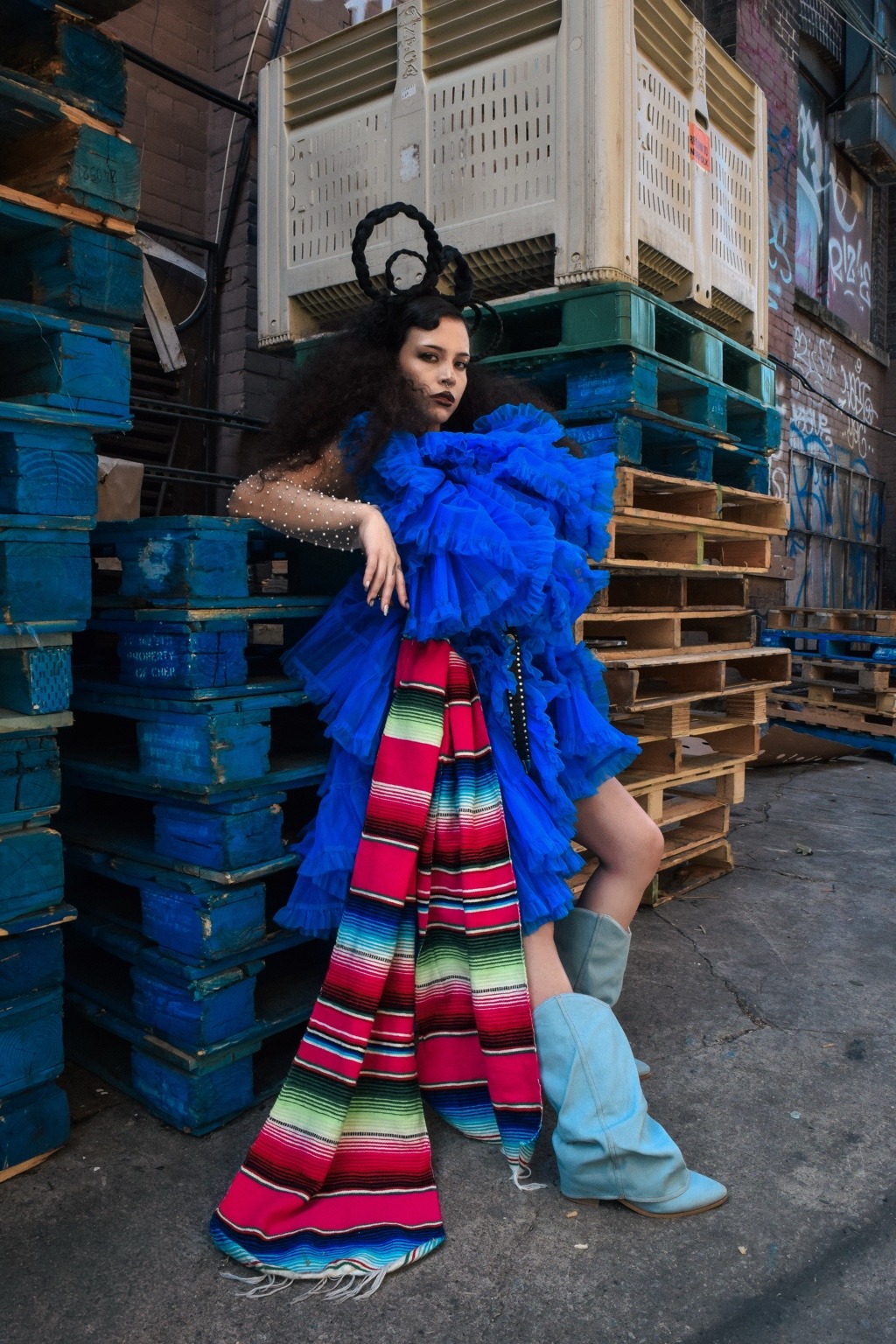 Look de tul azul y textil de rayas multicolores entre palés de madera.
