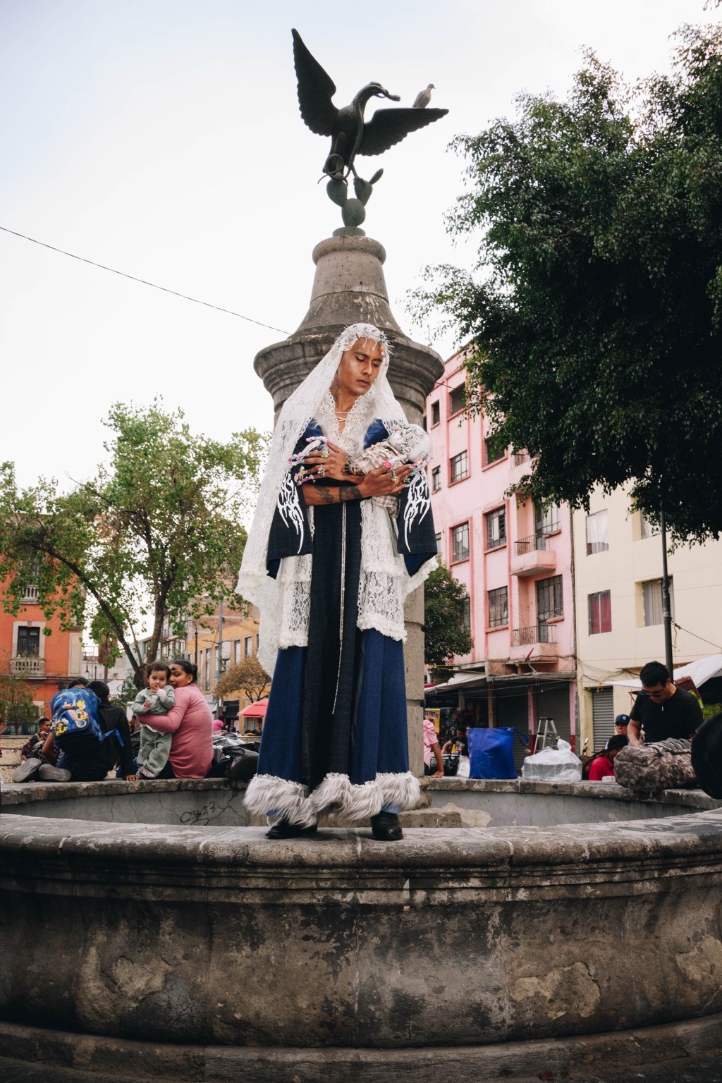 Modelo con velo blanco sostiene una figura frente al monumento de una fuente.