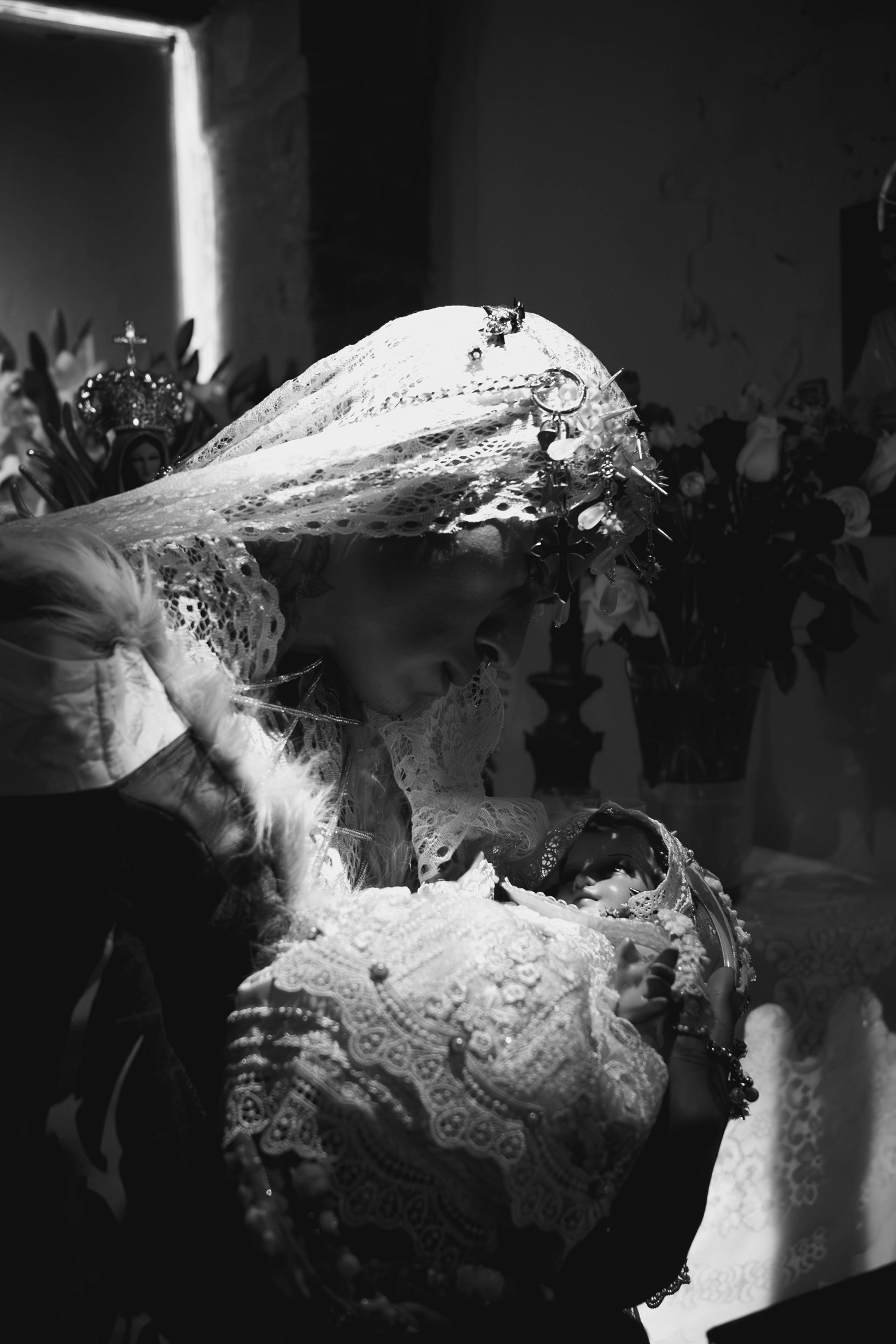 Fotografía en blanco y negro de un modelo con velo de encaje sosteniendo una figura del Niño Jesús en la capilla.
